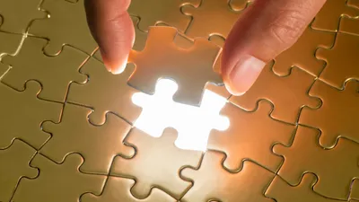 Zwei Finger setzen das letzte Teil in ein goldenes Puzzle; die Lücke leuchtet